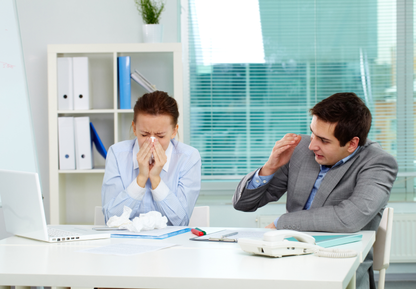 Image of businesswoman sneezing while her partner looking at her unsurely in office 